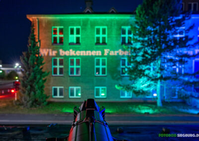 M4E Veranstaltungstechnik Referenz EvonikBlick über einen Gobo-Scheinwerfer auf eine beleuchtete Fassade. Auf die Fassade wird mit einem Gobo der Schriftzug "Wir bekennen Farbe" projiziert.