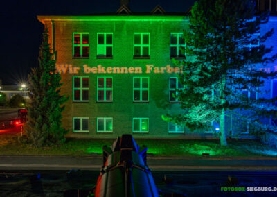 Blick über einen Gobo-Scheinwerfer auf eine beleuchtete Fassade. Auf die Fassade wird mit einem Gobo der Schriftzug "Wir bekennen Farbe" projiziert.