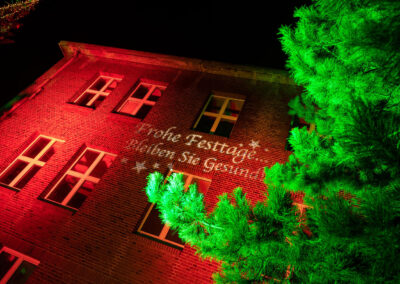 Kontrastreiche Beleuchtung einer Fassade in roter Farbe, Der Tannenbaum davor wurde grün angestrahlt. Stimmungsvolle Weihnachtsbeleuchtung der Evonik.