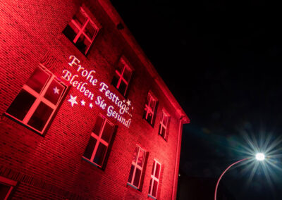 Weiße Gobo-Projektion "Frohe Festtage" auf die rot angestrahlte Fassade der Evonik Industries in Siegburg.