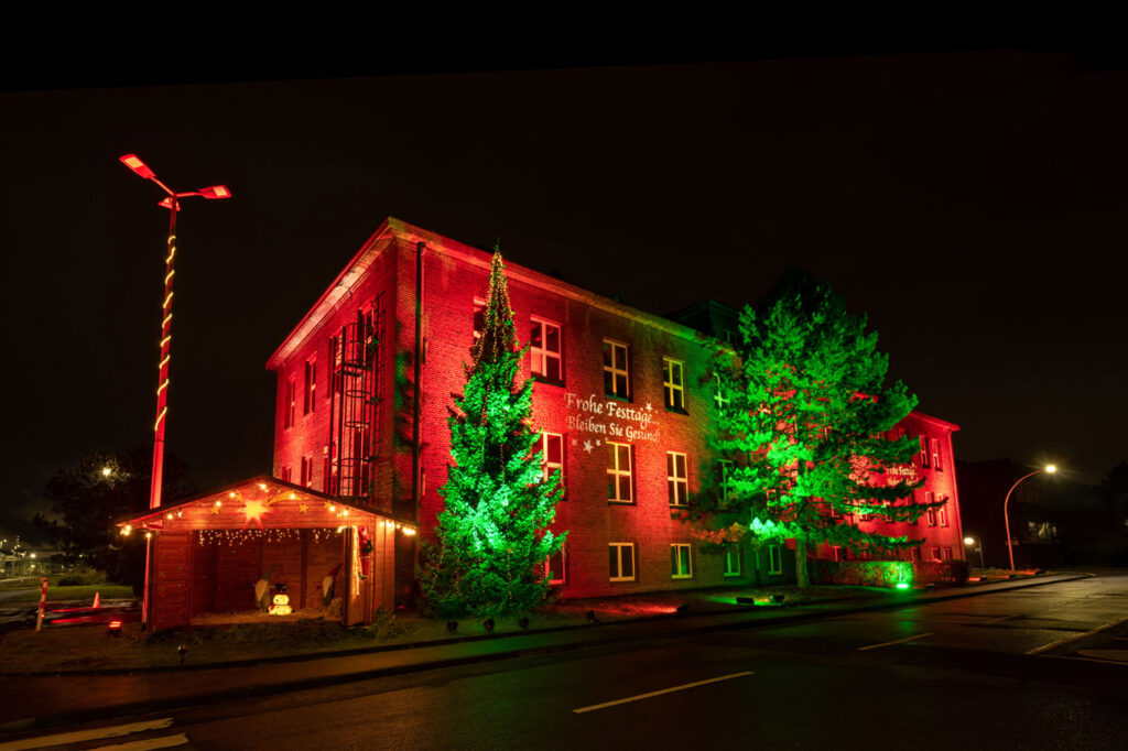 Das Gebäude der EVONIK mit einer weihnachtlichen Illumination von M4E Veranstaltungstechnik. Das Gebäude ist rot angestrahlt und die Bäume davor in grünes Licht getaucht.