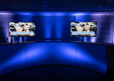 Eine in dunkelblaues Licht gehüllte Moderatorentheke auf denen zwei Monitore mit Bildern für ein Video Streaming stehen.