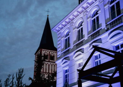 Violett illuminierte Gründerzeitfassade vor der Siegburger Kirche. Eine Installation von M4E Veranstaltungstechnik.